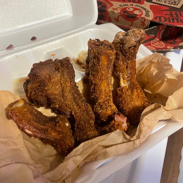 Crispy fried ribs in a white takeout container lined with brown paper, with a menu in the background.