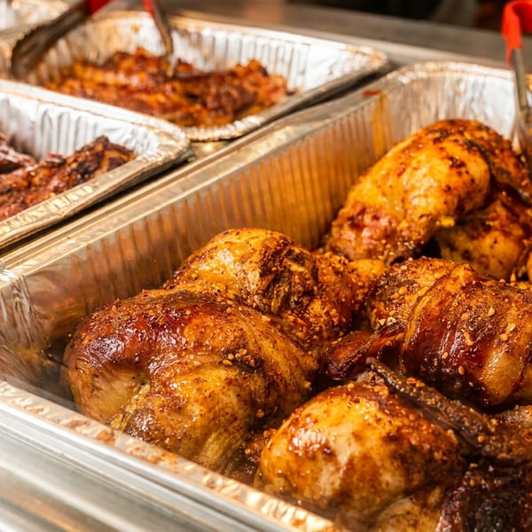 Two foil pans filled with barbecue chicken and ribs, ready for serving.