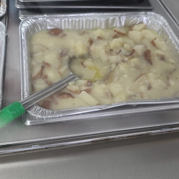 Creamy mashed potatoes with red skins in a foil pan, with a serving spoon.